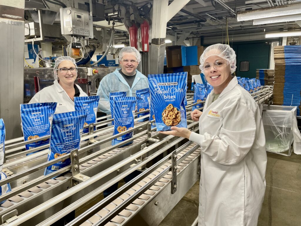 campbell snacks employees smiling next to snack factory pretzel crisps