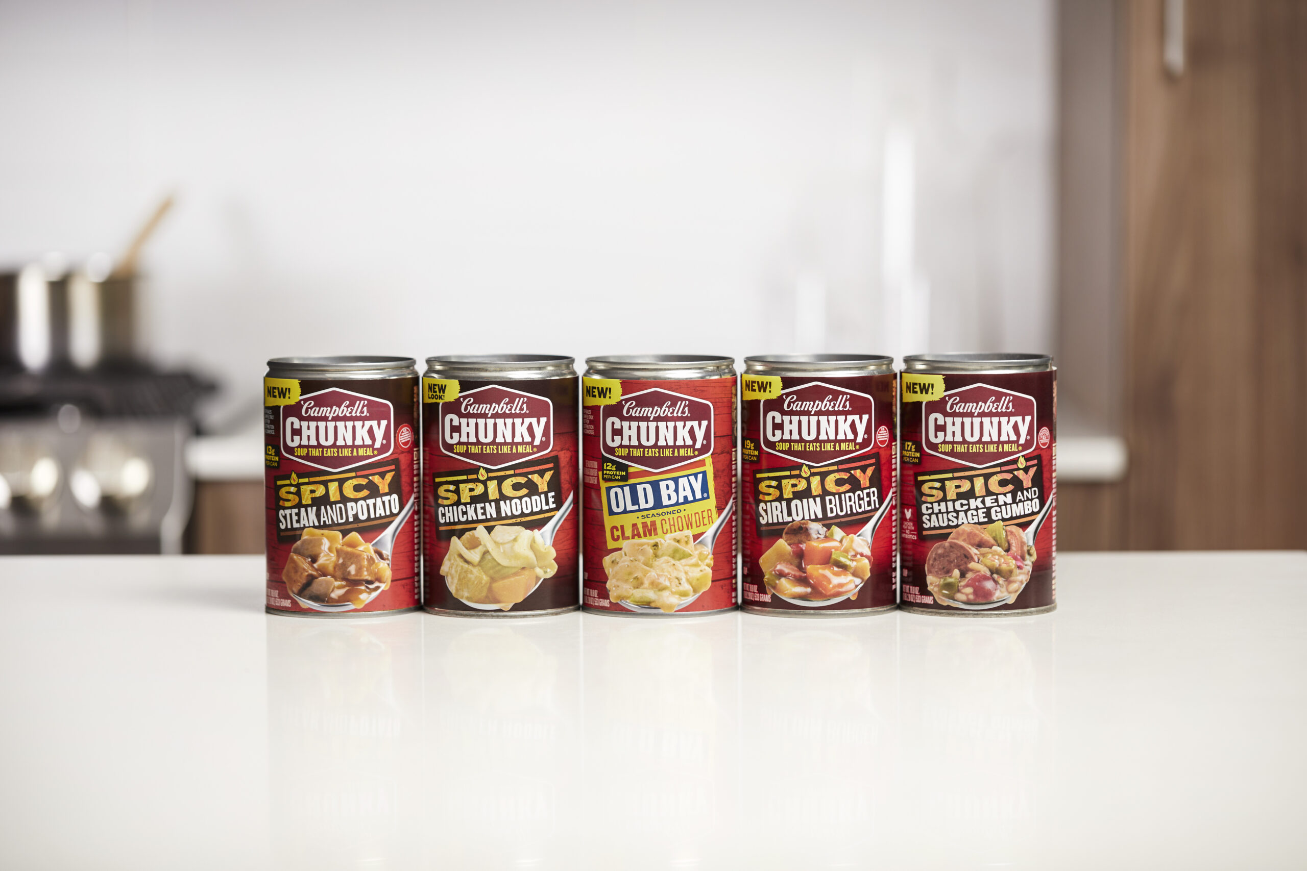 Lined up cans of Chunky soup, including Spicy Steak and Potato, Spicy Chicken Noodle, OLD BAY Seasoned Clam Chowder, Spicy Sirloin Burger, and Spicy Chicken and Sausage Gumbo